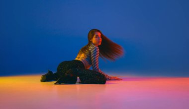 Warming up. Portrait of young girl dancing heels dance in stylish clothes over blue background in neon light. Concept of dance lifestyle, modern style, contemporary, youth culture, self-expression