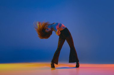 Portrait of young, dancer, girl dancing heels dance in stylish clothes over blue background in neon light. Concept of dance lifestyle, modern style, contemporary, youth culture, self-expression
