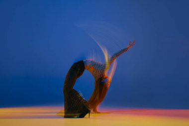 Mixed lights and flexibility. Portrait of young girl dancing heels dance on blue background in neon light. Concept of dance lifestyle, modern style, contemporary dance, youth culture, self-expression