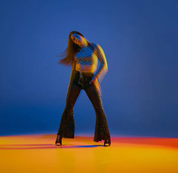 Young girl, heels dance performer in stylish clothes posing over blue background in neon with mixed lights. Concept of dance lifestyle, modern style, contemporary dance, youth culture, self-expression