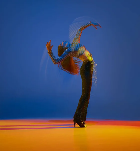 Portrait of young girl dancing heels dance in stylish clothes over blue background in neon with mixed lights. Concept of dance lifestyle, modern style, contemporary, youth culture, self-expression