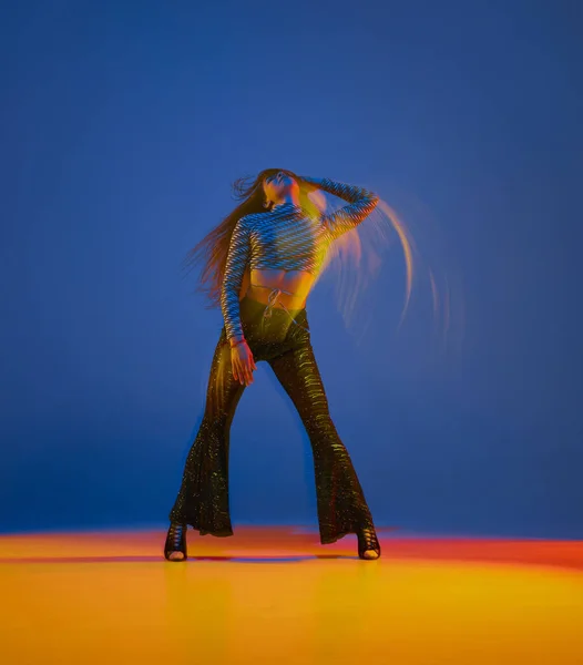Sensual young girl dancing heels dance in stylish clothes over blue background in neon with mixed lights. Concept of dance lifestyle, modern style, contemporary dance, youth culture, self-expression