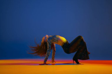 Flexibility and passion. Young girl dancing heels dance over blue background in neon with mixed lights. Concept of dance lifestyle, modern style, contemporary dance, youth culture, self-expression