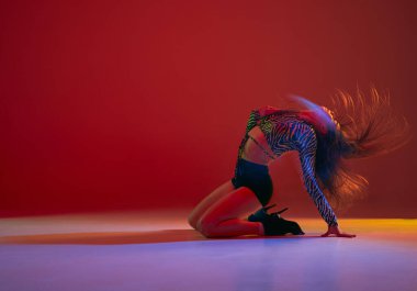 Passion and sensuality. Portrait of young girl dancing heels dance over red background in neon with mixed light. Concept of dance lifestyle, modern style, contemporary, youth culture, self-expression