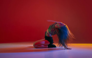Flexibility. Portrait of young girl dancing heels dance over red background in neon with mixed light. Concept of dance lifestyle, modern style, contemporary dance, youth culture, self-expression