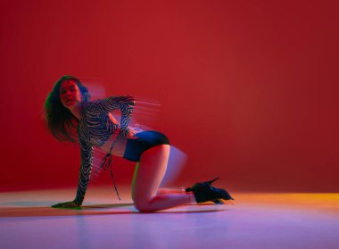 Passion, femininity. Portrait of young girl dancing heels dance on red background in neon with mixed light. Concept of dance lifestyle, modern style, contemporary dance, youth culture, self-expression
