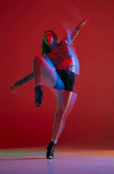 Balancing. Portrait of young girl dancing heels dance over red background in neon with mixed light. Concept of dance lifestyle, modern style, contemporary dance, youth culture, self-expression