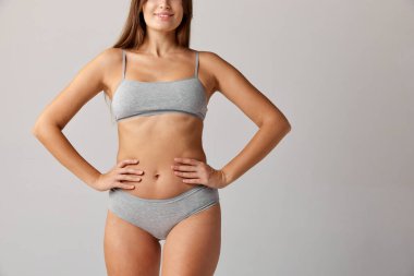 Cropped image of slim female body, breast, belly and buttocks in cotton underwear over grey studio background. Concept of body and skin care, fitness, natural beauty, health, wellness.