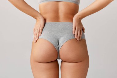 Cropped image of slim, fit female body, buttocks in cotton underwear over grey studio background. Anti-cellulite care. Concept of body and skin care, fitness, natural beauty, health, wellness.