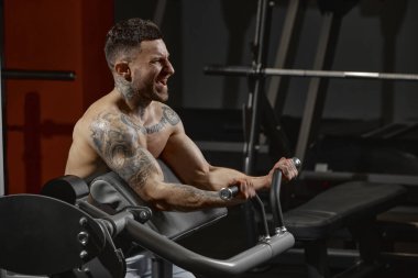 Portrait of young muscular man training shirtless in gym indoors. Hand exercises. Workout. Concept of health, sportive lifestyle, fitness, body care, diet, strength