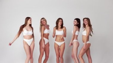 Positivity. Group of young beautiful girls posing, dancing in white underwear over grey studio background. Concept of body and skin care, fitness, natural beauty, wellness. Copy space for ad