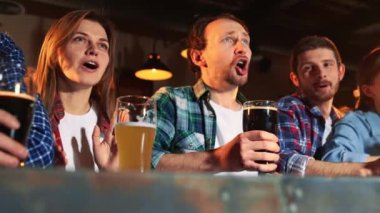 Group of young people, men and women watching match at pub, drinking beer. Fans emotionally cheering up favourite sport team. Happy. Competition, championship, match translation. Emotions. Win