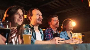 Group of young people, men and women, Fans emotionally cheering up favourite sport team at the pub. Clinking beer glasses. Successful game. Competition, championship, match translation. Emotions.