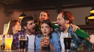 Group of young people, men and women watching match at pub. Fans emotionally cheering up favourite sport team. Friends meeting. Competition, championship, match translation. Emotions.