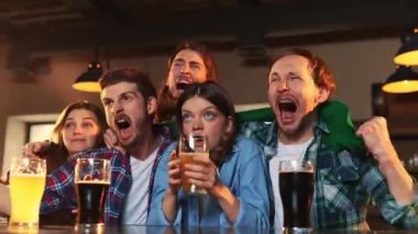 Group of emotive young people, men and women watching match at pub. Fans emotionally cheering up favourite sport team. Attentive look. Competition, championship, match translation. Emotions.