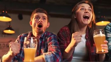 Group of young people, men and women watching match at pub and drinking beer. Fans emotionally cheering up favourite sport team. Competition, championship, match translation. Emotions.