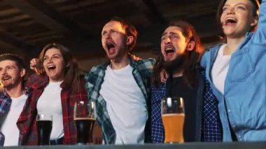 Group of young people, men and women watching match at pub. Fans emotionally cheering up favourite sport team. Celebrating winning game. Competition, championship, match translation. Emotions.
