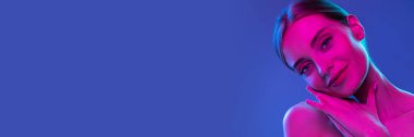 Beautiful young woman with perfect smooth skin over blue background in neon light. Cosmetological skin care. Concept of cosmetics, plastic surgery, natural beauty. Banner, flyer. Copy space for ad
