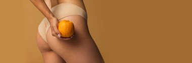 Cropped image of slim smooth female legs, buttocks with orange over light brown background. Anti-cellulite care. Concept of body, skin care, fitness, health, wellness. Banner, flyer. Copy space for ad