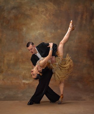 Expressive couple dance. Man and woman, professional dancers in stylish, beautiful stage costumes performing ballroom dance over dark vintage background. Concept of hobby, lifestyle, action, motion.