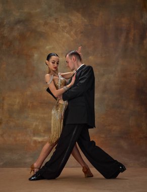 Man and woman, professional tango dancers in stylish, beautiful stage costumes performing over dark vintage background. Couple dance style. Concept of hobby, lifestyle, action, motion.