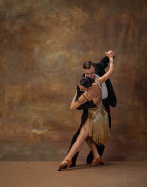 Femininity and masculinity. Man and woman, professional tango dancers in stylish, beautiful stage costumes performing over dark vintage background. Concept of hobby, lifestyle, action, motion.
