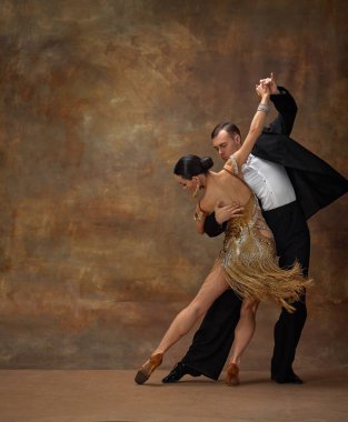 Man and woman, professional tango dancers in stylish stage costumes performing over dark vintage background. Self-expression. Art. Concept of hobby, lifestyle, action, motion, dance aesthetics