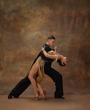Passion, emotions. Man and woman, professional tango dancers in stylish, beautiful stage costumes performing over dark vintage background. Concept of hobby, lifestyle, action, motion, dance aesthetics