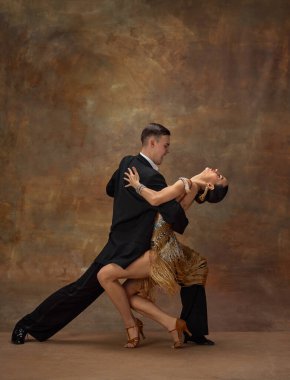 Man and woman, professional tango dancers in stylish, beautiful stage costumes performing over dark vintage background. Passionate performance. Concept of hobby, lifestyle, motion, dance aesthetics