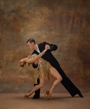 Man and woman, professional tango dancers in stylish, beautiful stage costumes performing over dark vintage background. Atrraction. Concept of hobby, lifestyle, action, motion, dance aesthetics