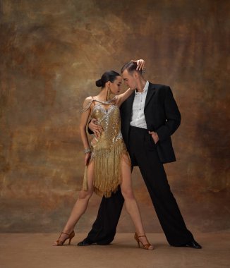 Man and woman, professional tango dancers in stylish, beautiful stage costumes performing on dark vintage background. Romance and passion. Concept of hobby, lifestyle, action, motion, dance aesthetics