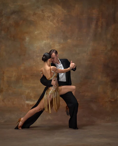 Attractive man and woman, professional dancers performing ballroom dance in stylish, beautiful costumes over dark vintage background. Passion. Concept of hobby, lifestyle, action, motion. Couple dance