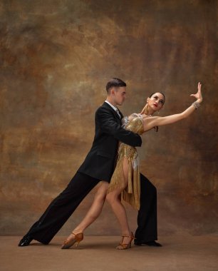 Young man and woman, professional tango dancers in stylish, beautiful stage costumes performing over dark vintage background. Concept of hobby, lifestyle, action, motion, dance aesthetics