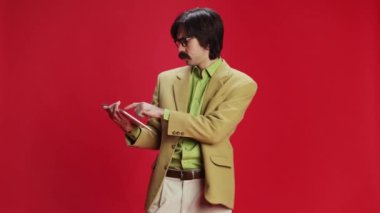 Man, businessman in retro classic suit looking on tablet, showing perfect project idea on screen over red background. Concept of emotions, business, occupation, facial expression, fashion