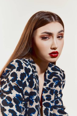 Modern style. Young beautiful girl with straight brown hair and red lips make up posing over grey studio background. Concept of natural beauty, youth, fashion, cosmetology, wellness, makeup.