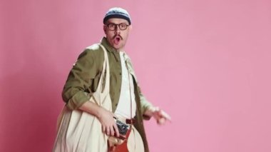 Inspired tourist. Emotive man in casual clothes walking and taking photo with vintage camera over pink studio background. Travelling. Concept of emotions, lifestyle, mens fashion, mood. Ad