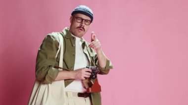 Amateur photographer, tourist. Stylish man in casual urban style clothes taking photos with vintage camera over pink studio background. Concept of emotions, lifestyle, mens fashion, mood. Ad