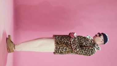 Stylish man in fashionable animal print fur coat, trendy sunglasses and necklace chain, dancing, posing over pink studio background. Concept of emotions, lifestyle, mens fashion, mood. Ad