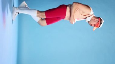 Emotive man in retro sportive clothes, bike shorts and cap posing over blue studio background. Coach, trainer cheering up. Concept of sportive lifestyle, emotions, retro style, fun, fashion. Ad