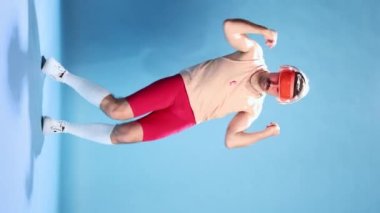 Funny dance moves. Emotive man in retro sportive clothes, bike shorts and cap posing over blue studio background. Concept of sportive lifestyle, emotions, retro style, fun, fashion. Ad