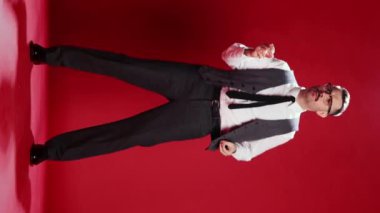 Handsome businessman in official classic suit dancing, posing over red studio background. Relaxation, positive mood. Concept of emotions, business, occupation, facial expression, fashion