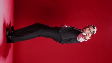 Handsome businessman in official classic suit dancing, posing over red studio background. Showing positivity and good vibes. Concept of emotions, business, occupation, facial expression, fashion