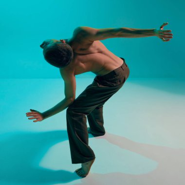 Contemporary dance style. Young man, professional contemp dancer, performing, dancing over blue, cyan studio background. Modern. Concept of art, body aesthetics, motion, action and inspiration.