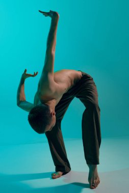 Contemporary dance style. Young shirtless flexible artistic man dancing, performing contemp over blue studio background. Self-expression. Concept of art, body aesthetics, motion, action, inspiration.