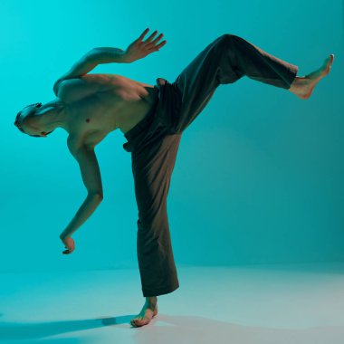 Contemporary dance style. Young shirtless, artistic man dancing contemp, experimental dance over blue, cyan studio background. Concept of art, body aesthetics, motion, action, inspiration.