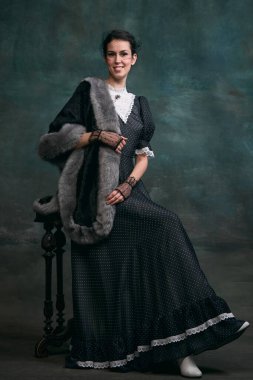 Beautiful woman in image of Anna Karenina in stylish dark dress posing over vintage dark green background. Concept of literature character, history, retro style, comparison of eras