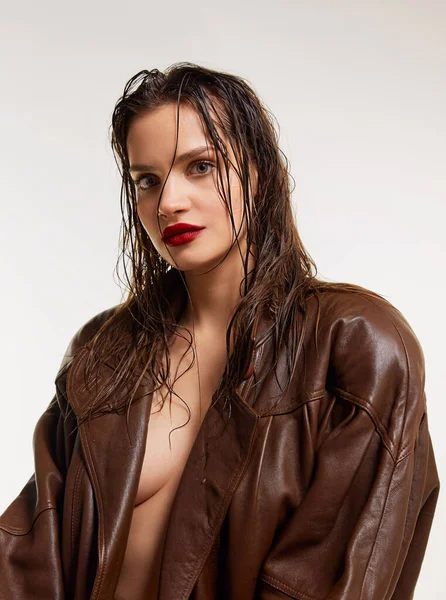 Sensual look with wet hair and red lips. Beautiful young brunette girl in stylish leather jacket posing on grey studio background. Concept of natural beauty, skin care, cosmetology, cosmetics, fashion
