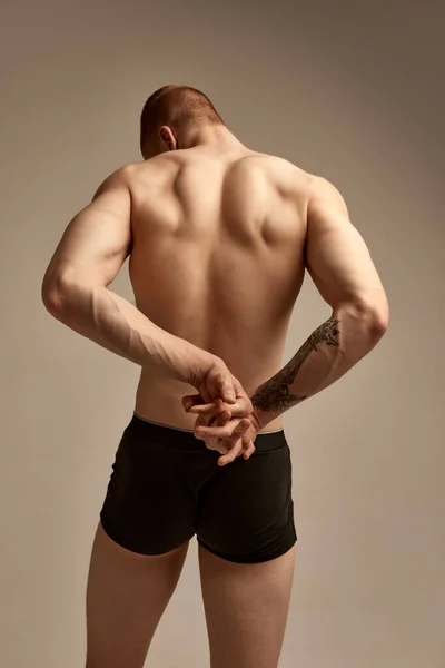 Veins on hands, strength. Male model posing in underwear over grey studio background. Relief, muscular back. Concept of mens health and beauty, body and skin care, fitness. Body art