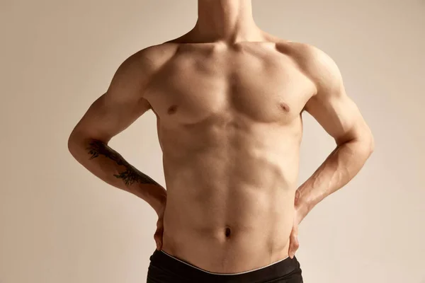 Cropped image of male relief body, breast, belly and hands over grey background. Model posing in underwear. Concept of mens health and beauty, body and skin care, fitness. Body art