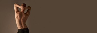 Gri stüdyo arka planında pantolonlu üstsüz bir gencin arka plan fotoğrafı. Güçlü, rahatlatıcı, kaslı vücut, sırt. Erkeklerin sağlık ve güzellik anlayışı, vücut bakımı, fitness. Pankart. İlan, metin için boşluk kopyala